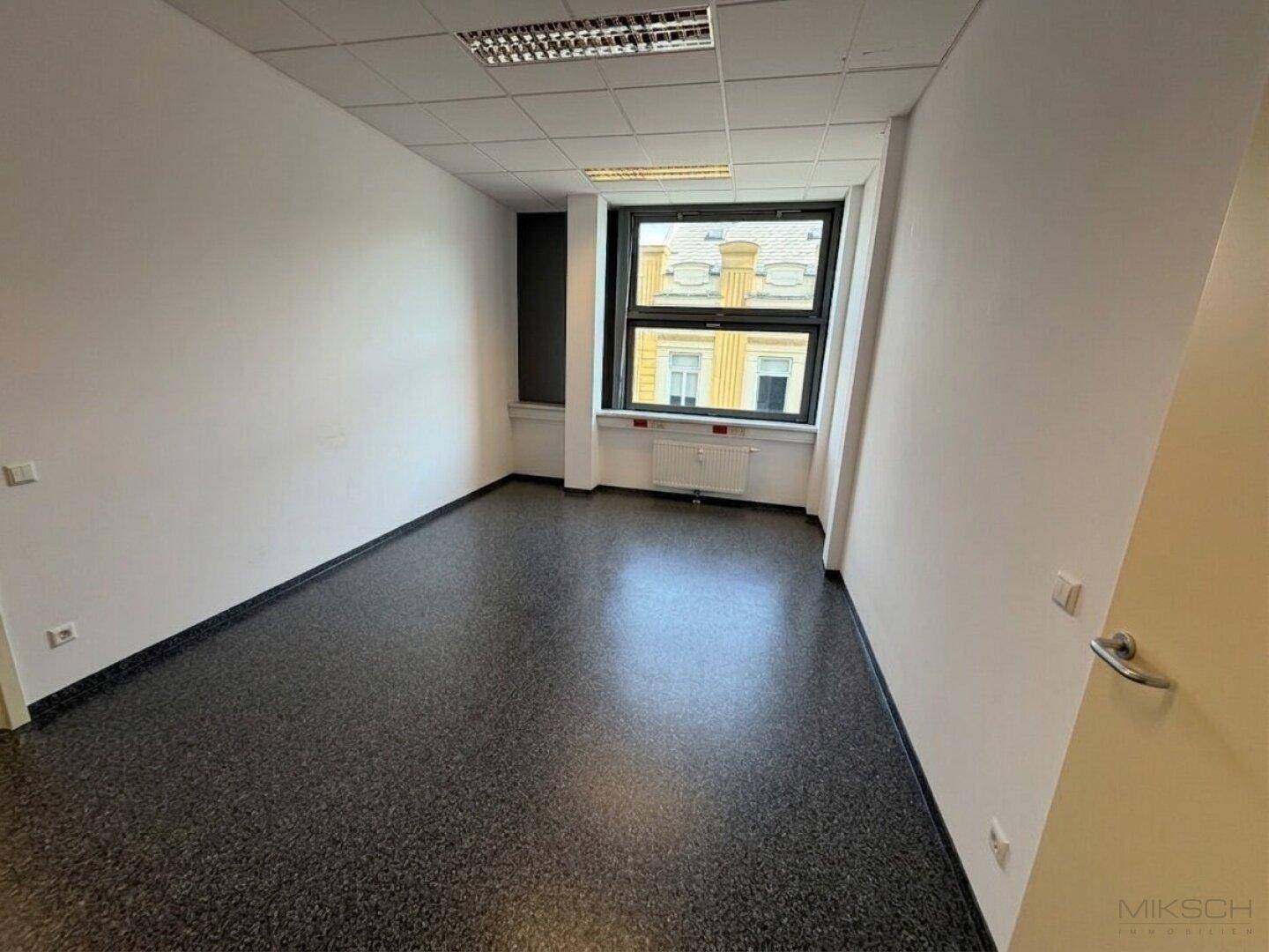 Funktionales Einzelbüro mit einem Fenster und dunklem Vinylboden, ideal für konzentriertes Arbeiten in ruhiger Umgebung.