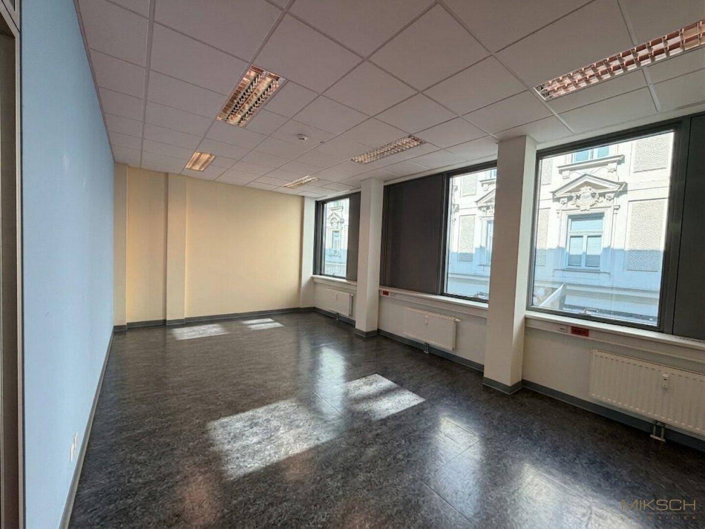 Geräumiges Büro mit mehreren Fenstern, die eine helle Arbeitsatmosphäre schaffen und einen angenehmen Stadtblick bieten.