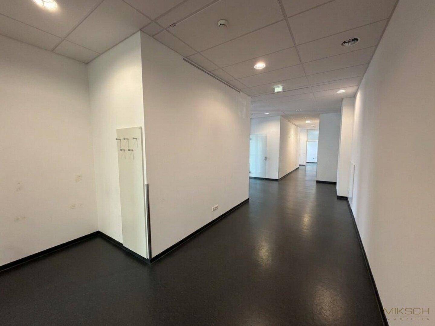 Heller Flur mit Garderobenbereich und durchgehenden Vinylböden, der zu weiteren Büros und Räumen führt.