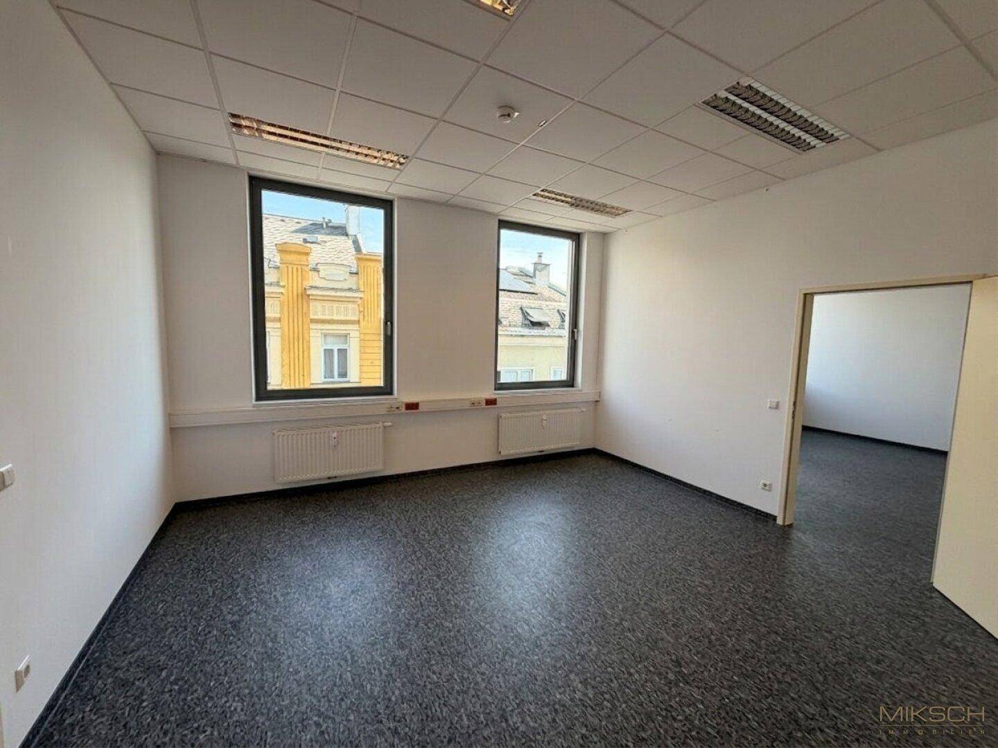 Helles Büro mit zwei Fenstern, die einen Blick auf die umliegenden Gebäude und Dächer freigeben und viel Licht spenden.