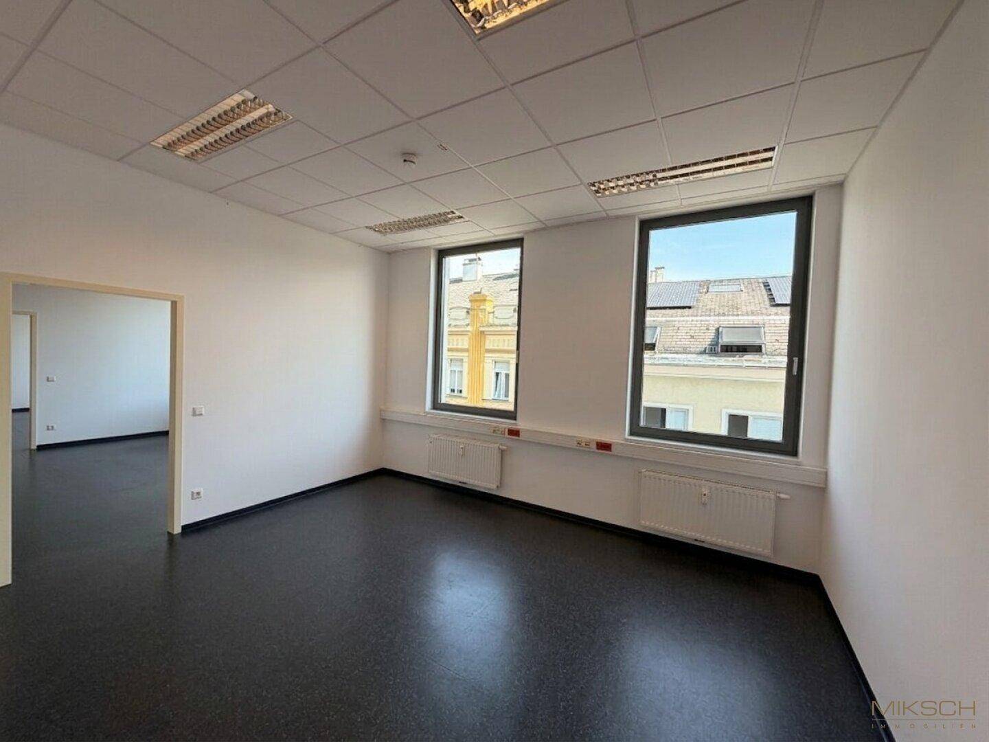 Funktionales Büro mit zwei Fenstern und dunklem Boden, das eine angenehme Arbeitsumgebung in der oberen Etage bietet.