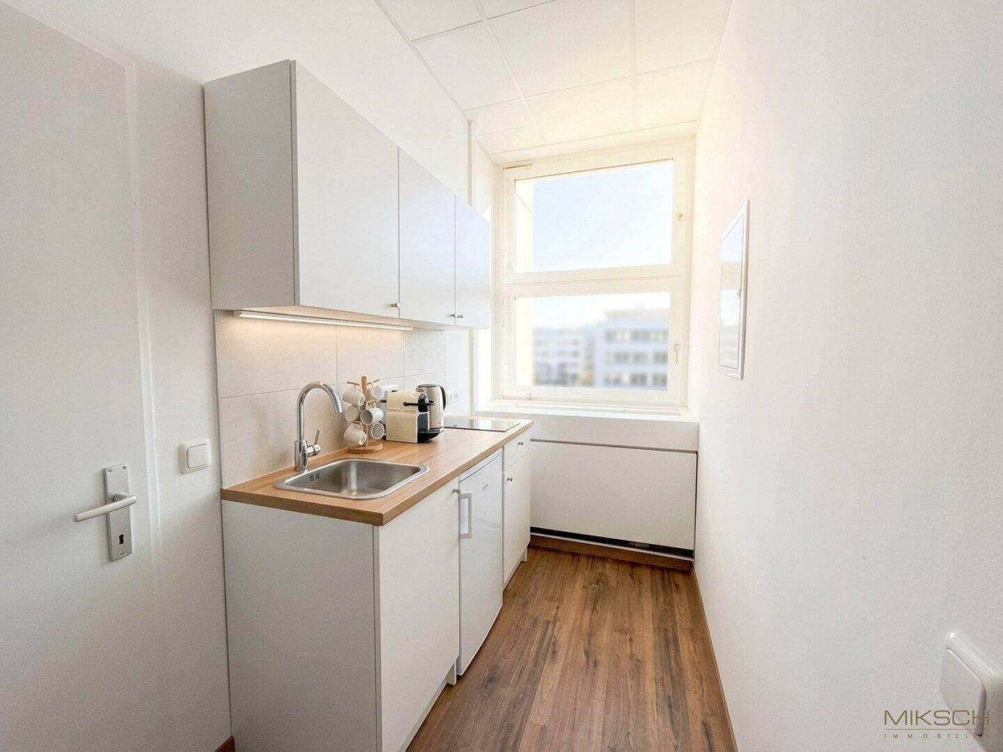 Kleine, moderne Küchenzeile mit weißen Schränken, Holztheke und Fenster.