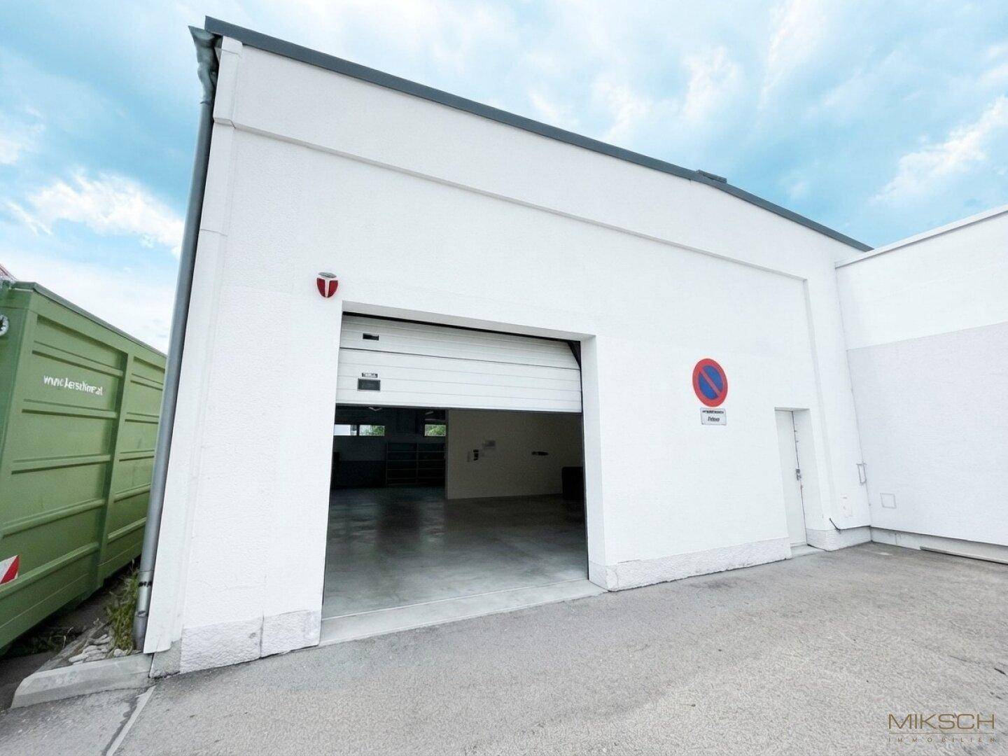 Außenansicht eines modernen Gewerbegebäudes mit großem Rolltor und angrenzendem Parkplatz.