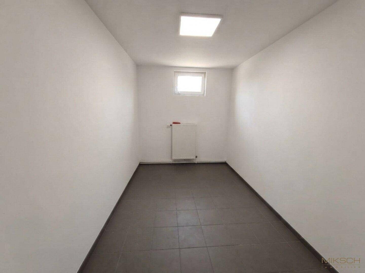 Kleiner, leerer Abstellraum mit Fliesenboden, einem Fenster und einem Heizkörper an der Wand.