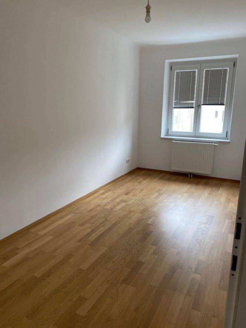 Heller Raum mit Holzboden und Fenster mit Jalousien, geeignet als Schlafzimmer.