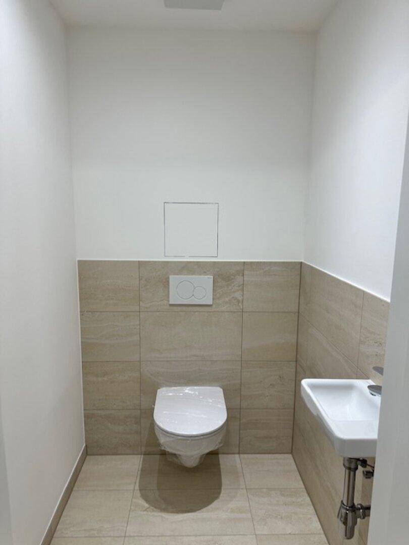 Kleines Gäste-WC mit beigefarbenen Fliesen, wandhängender Toilette und kompaktem Waschbecken.