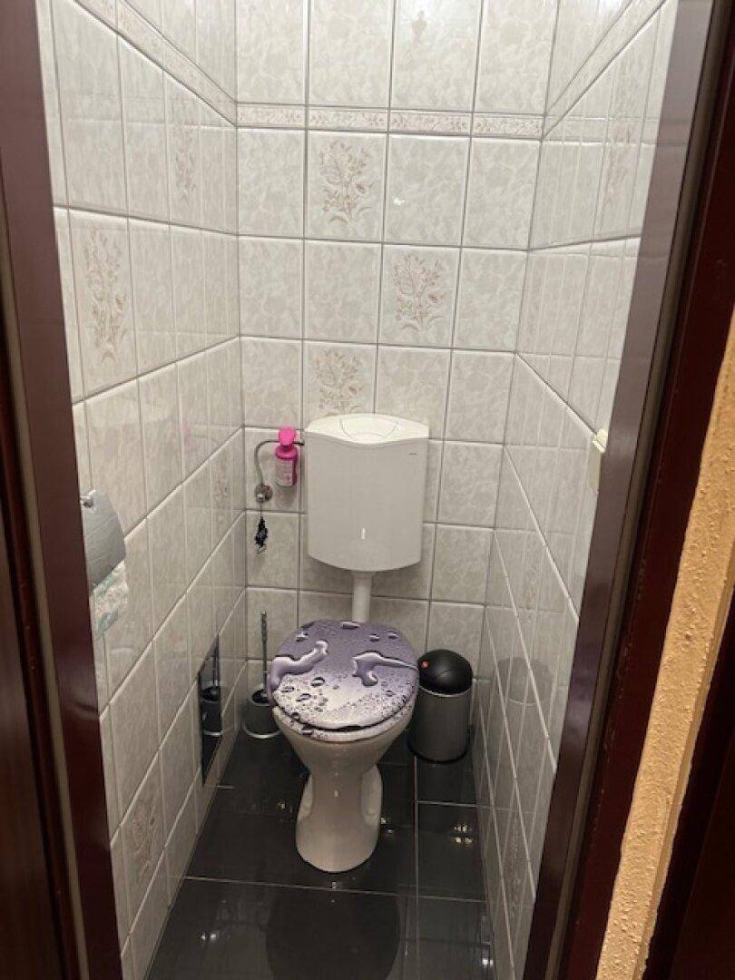 Kleines Gäste-WC mit weißen Fliesen an den Wänden und dunklem Boden.