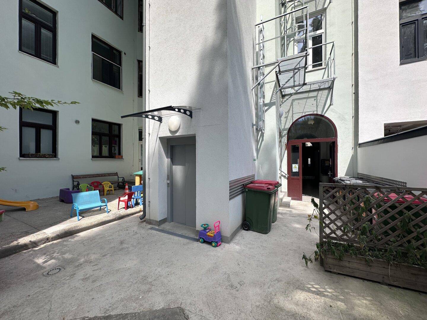 Innenhof mit kleinem Spielbereich, Aufzugzugang und Mülltonnen.