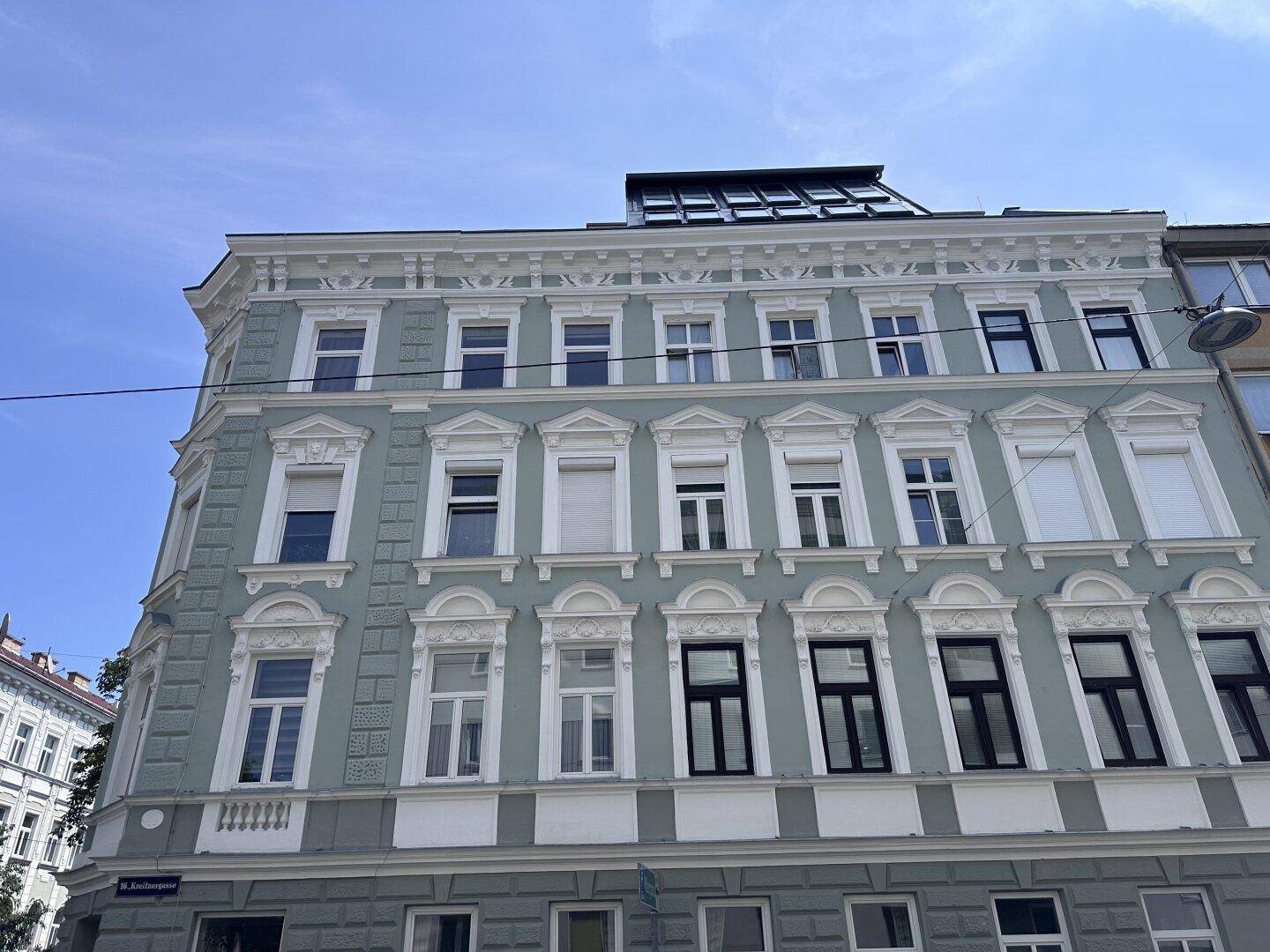 Historische Fassade eines Mehrfamilienhauses mit vielen Fenstern und dekorativen Elementen.