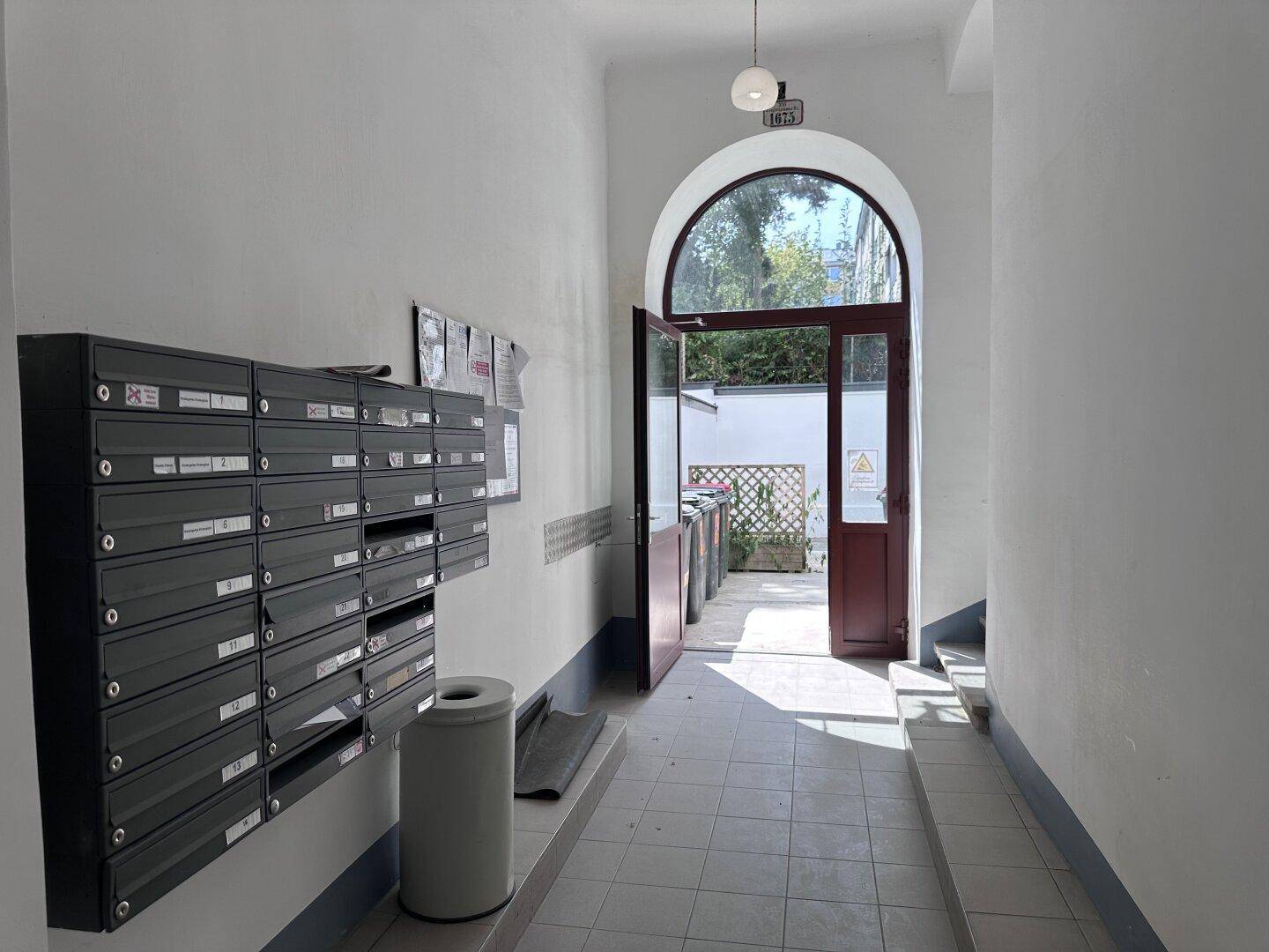 Heller Eingangsbereich mit Briefkästen, Fliesenboden und einem Bogenfenster zum Innenhof.
