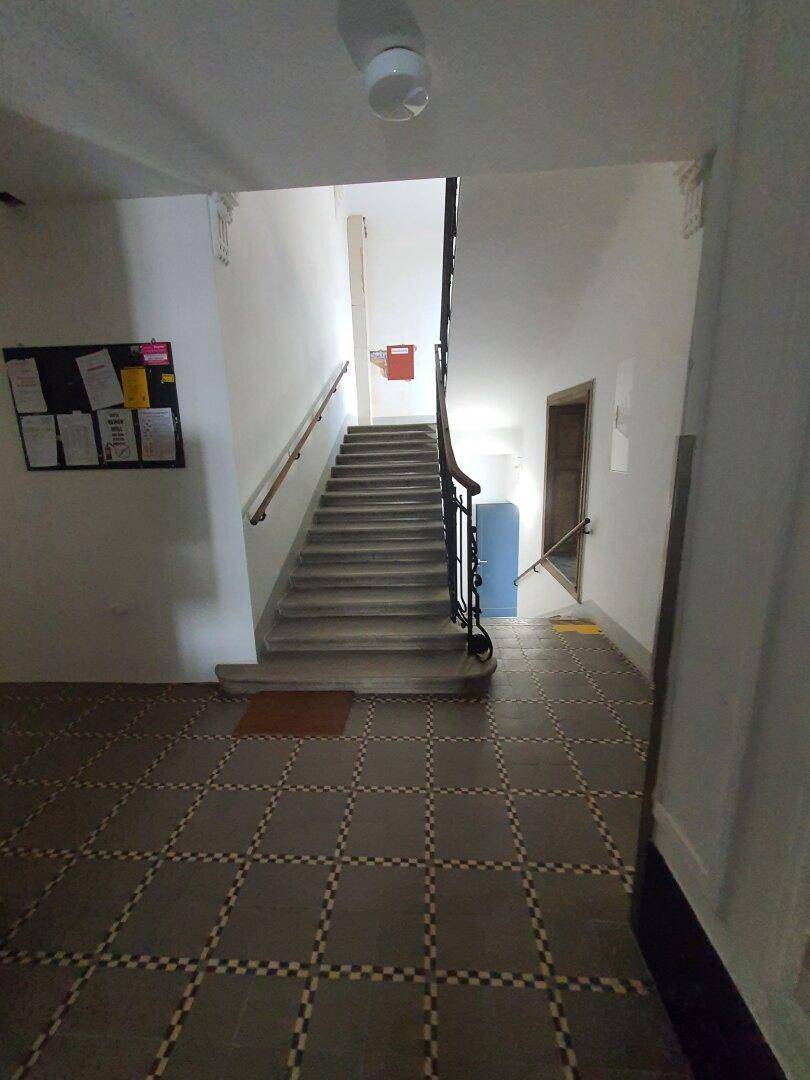 Helles Treppenhaus mit gemusterten Fliesen, weiß gestrichenen Wänden und einem Holzgeländer.
