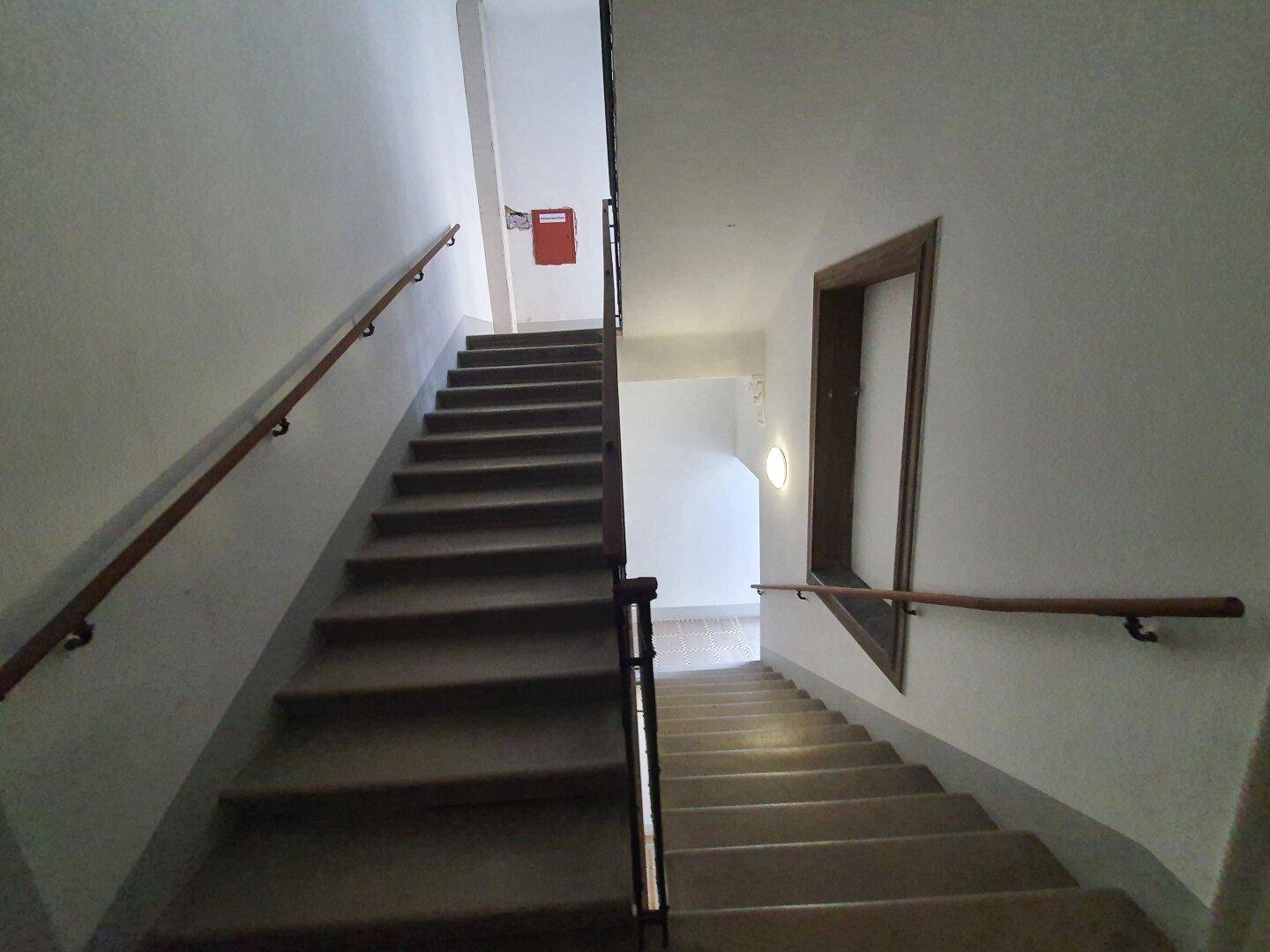 Aufwärtsblick in ein helles Treppenhaus mit mehreren Etagen und Holzhandläufen.