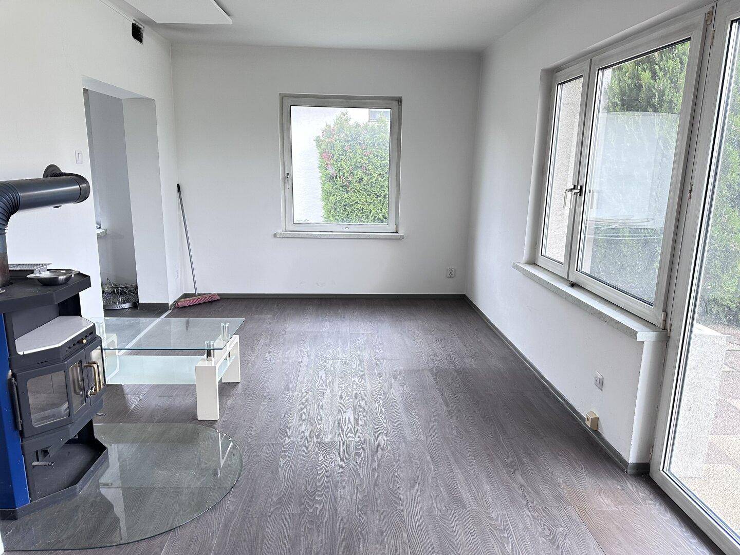Helles Wohnzimmer mit dunklem Laminatboden, Kaminofen und Blick in den Garten.