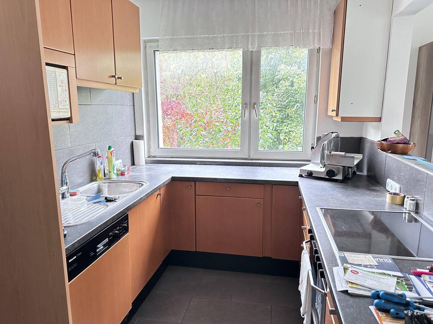 Funktionale Küche mit Holzschränken, dunkler Arbeitsplatte und Fenster mit Blick ins Grüne.