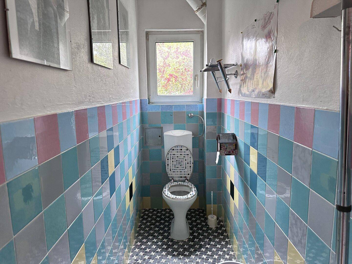 Separate Toilette mit farbenfrohen Fliesen und einem Fenster für natürliche Belüftung.