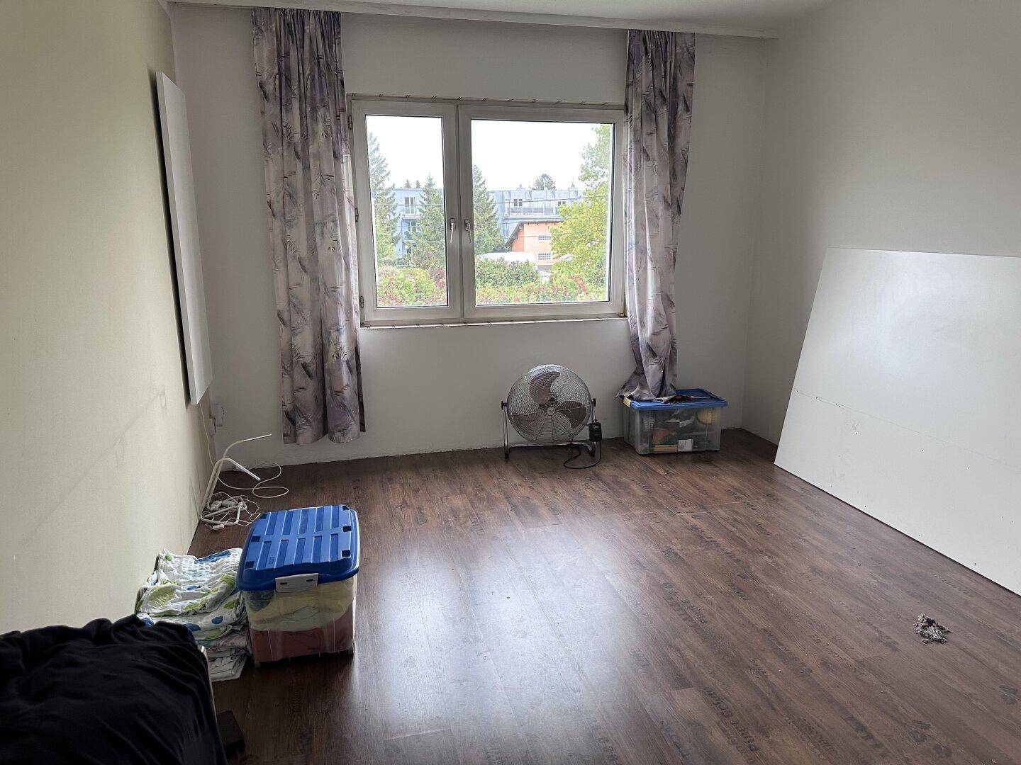 Schlafzimmer mit dunklem Laminatboden und großem Fenster, das viel Tageslicht hereinlässt.