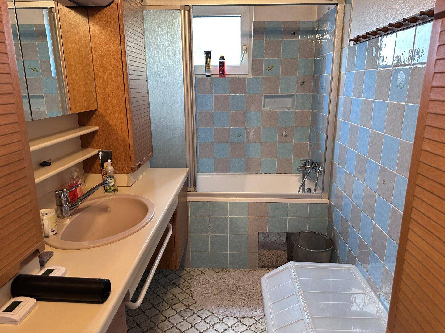Badezimmer mit Badewanne, Waschbecken und hellblauen sowie grauen Fliesen im Retro-Stil.