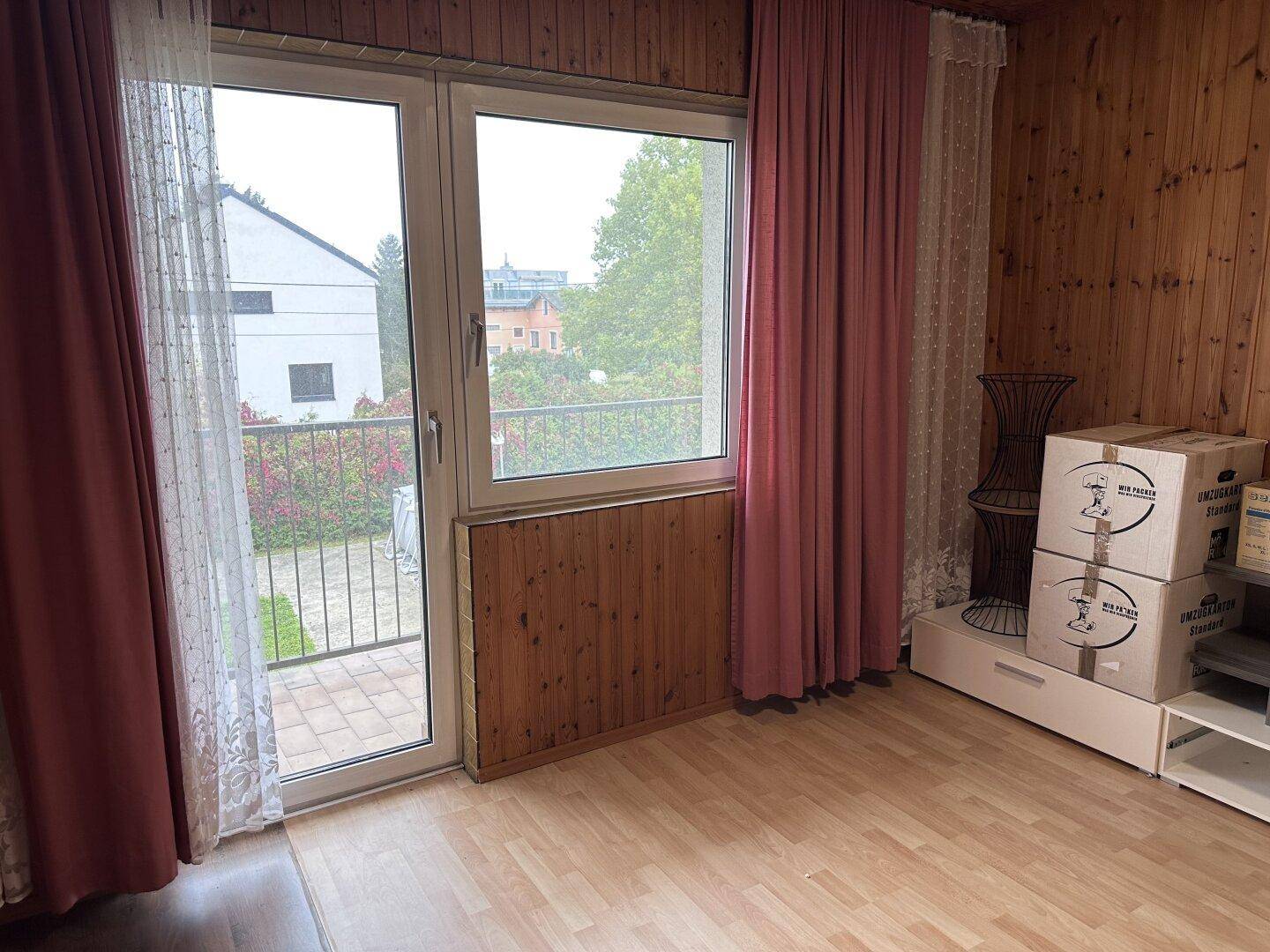 Schlafzimmer mit Holzwänden, hellem Laminatboden und Zugang zu einem Balkon.