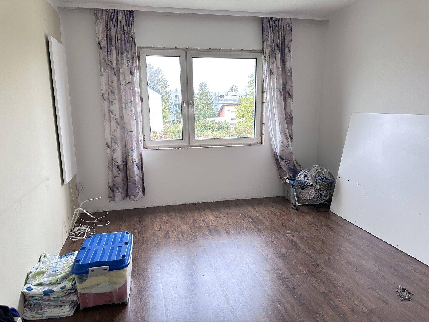 Schlafzimmer mit dunklem Laminatboden und großem Fenster, das viel Tageslicht hereinlässt.
