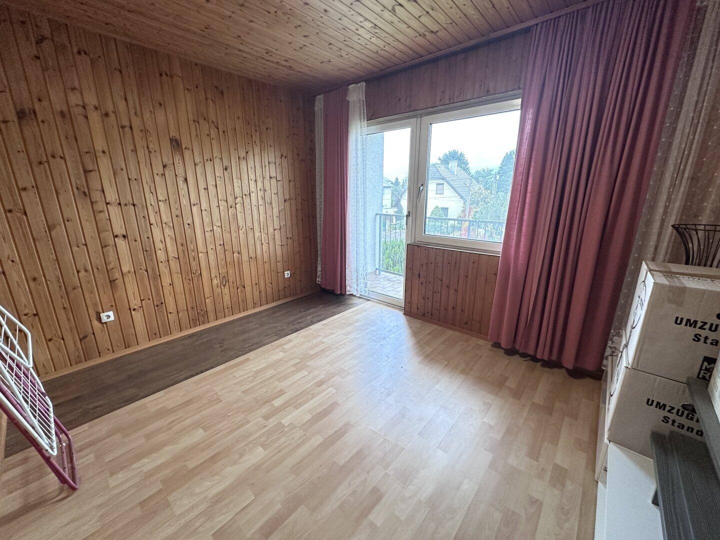 Geräumiges Zimmer mit Holzvertäfelung, Laminatboden und Zugang zu einem Balkon.