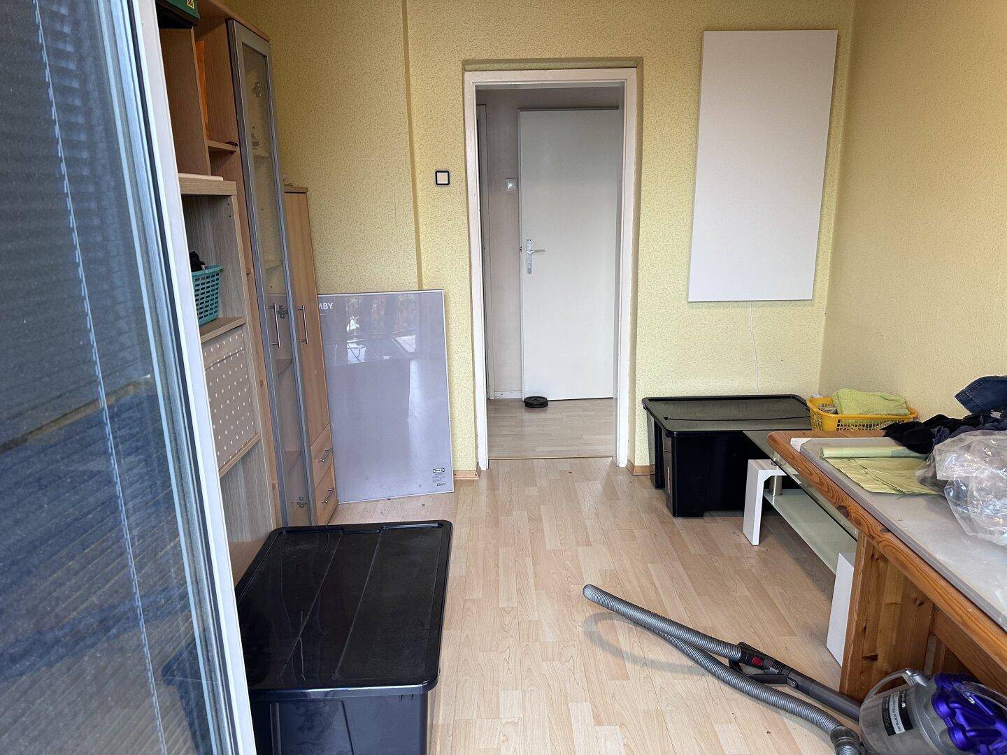 Innenraum mit Laminatboden, Regalen und Blick auf eine offene Tür zu einem weiteren Raum.