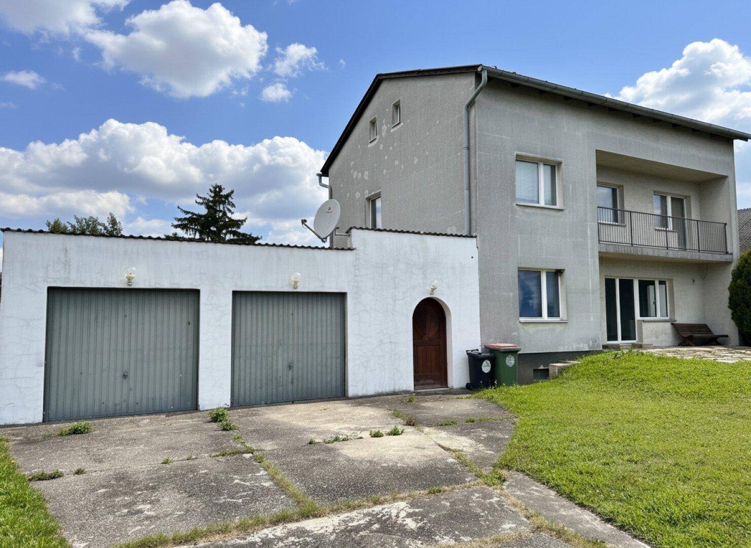 Ansicht des Hauses mit Doppelgarage und gepflegtem Vorgarten unter blauem Himmel.