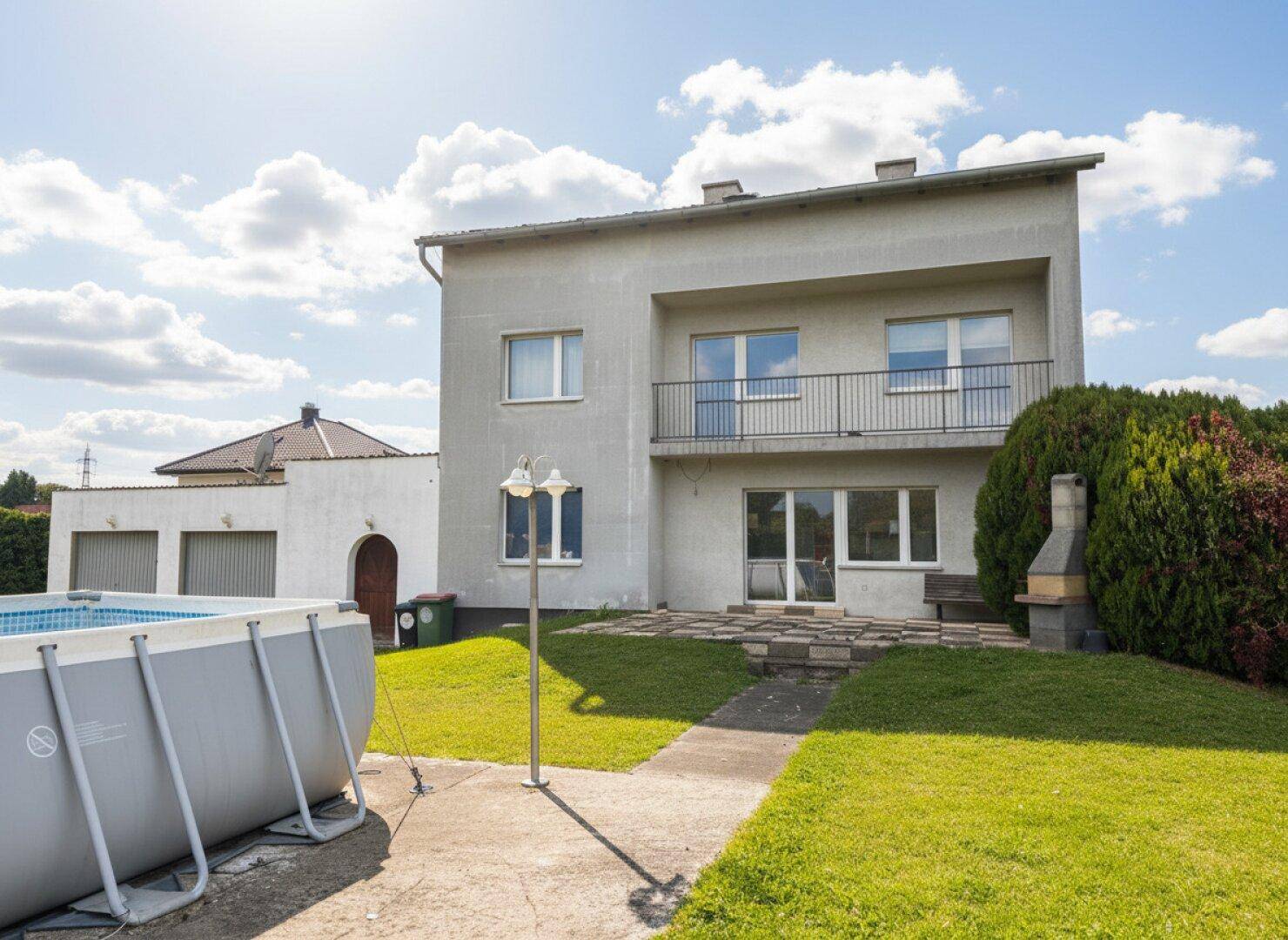 Rückansicht des Hauses mit Terrasse, Garten und einem Aufstellpool unter blauem Himmel.