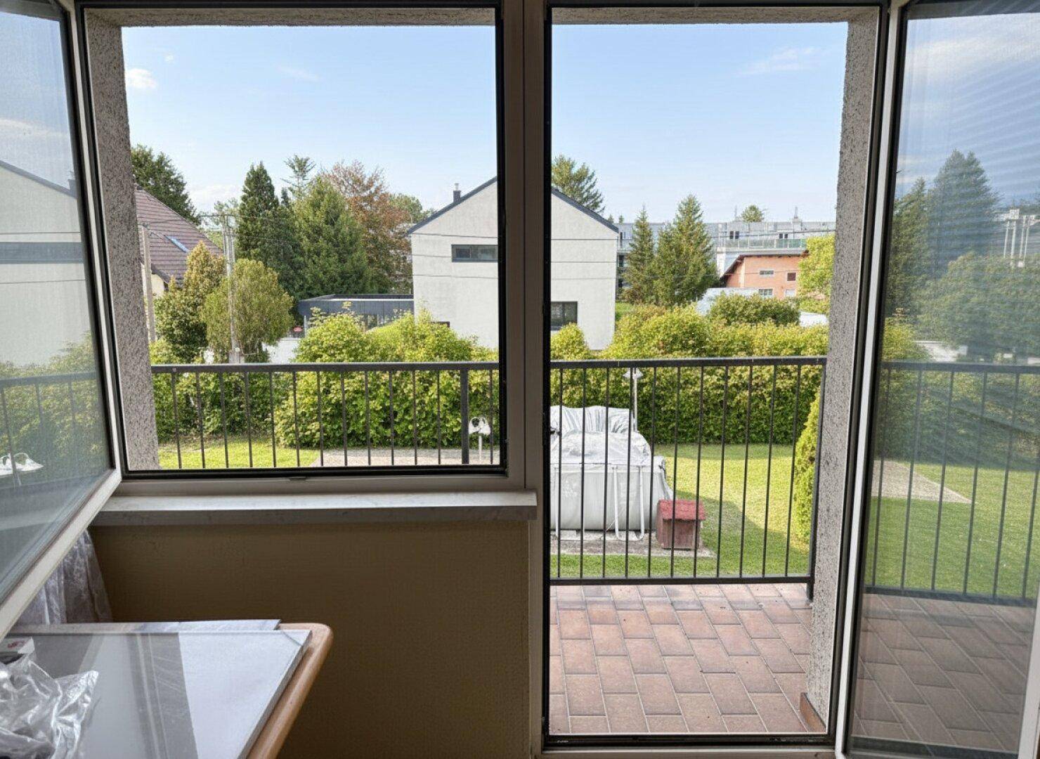 Blick vom Balkon auf den grünen Garten mit Aufstellpool und die umliegende Wohngegend.