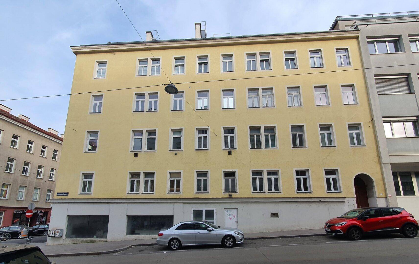 Gelbes Mehrfamilienhaus mit vielen Fenstern an einer städtischen Straße.