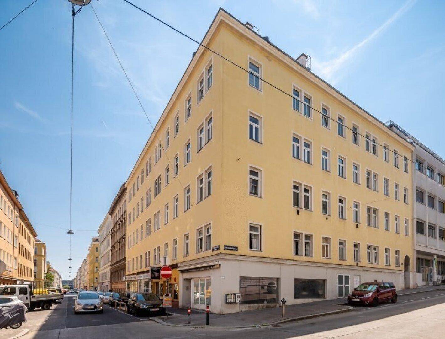 Gelbes Eckgebäude in städtischer Umgebung unter blauem Himmel.