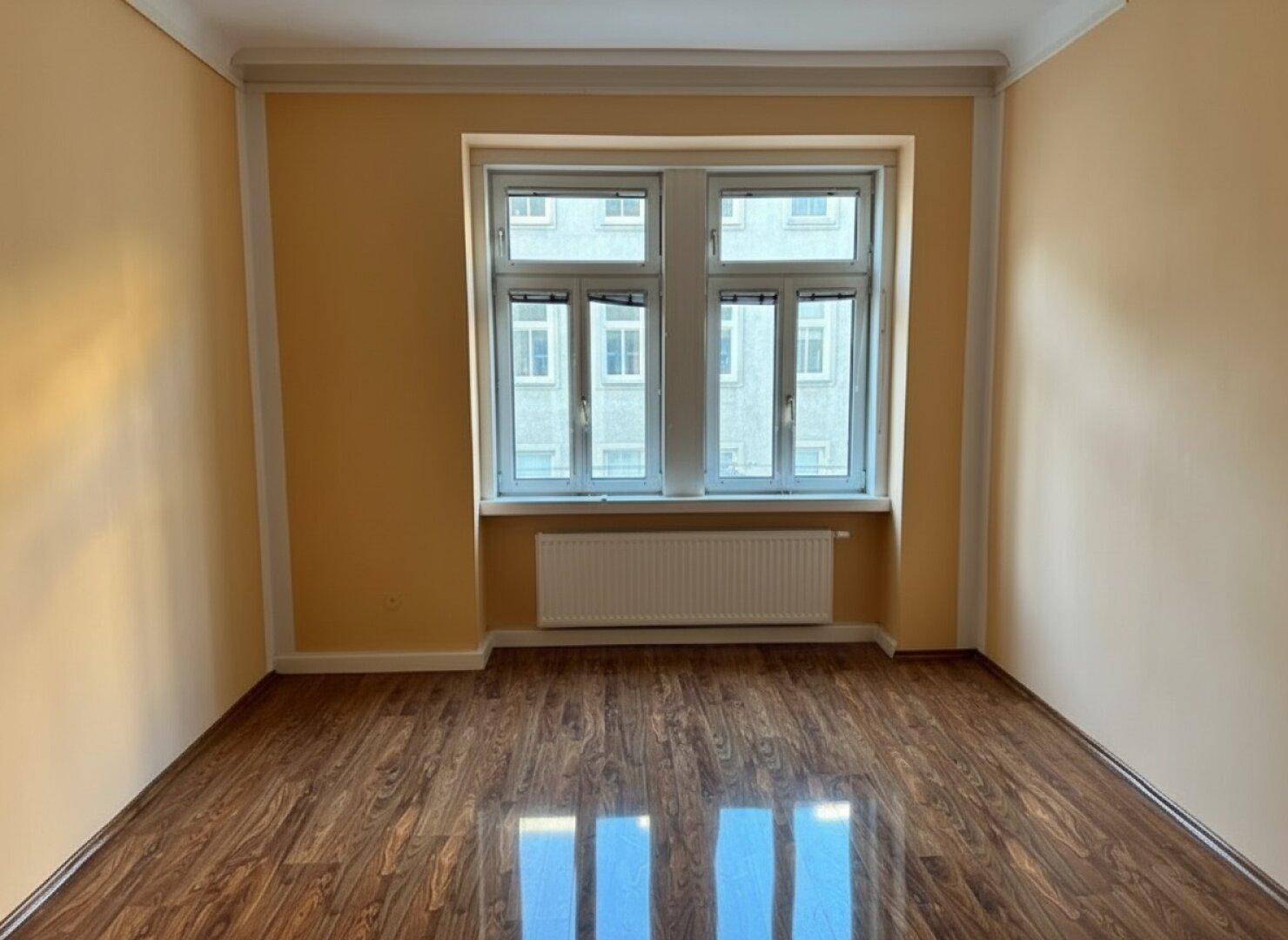 Gemütliches Zimmer mit gelben Wänden, Laminatboden und einem großen Fenster.