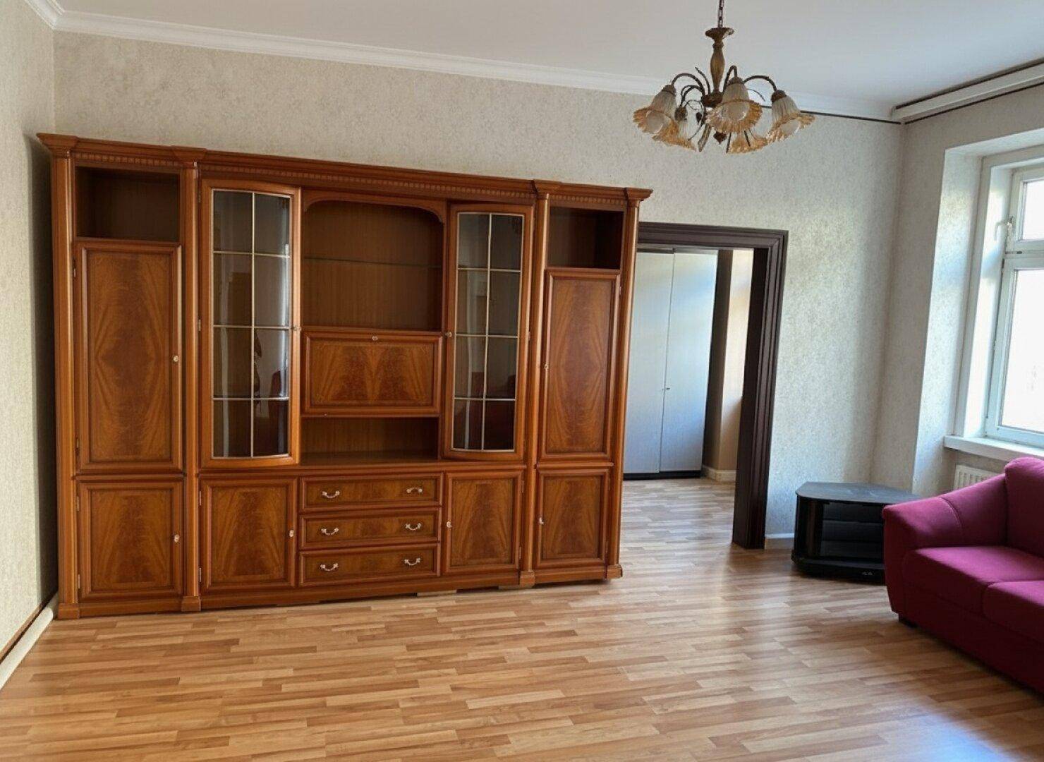 Geräumiges Wohnzimmer mit großer Holzschrankwand, rotem Sofa und Laminatboden.
