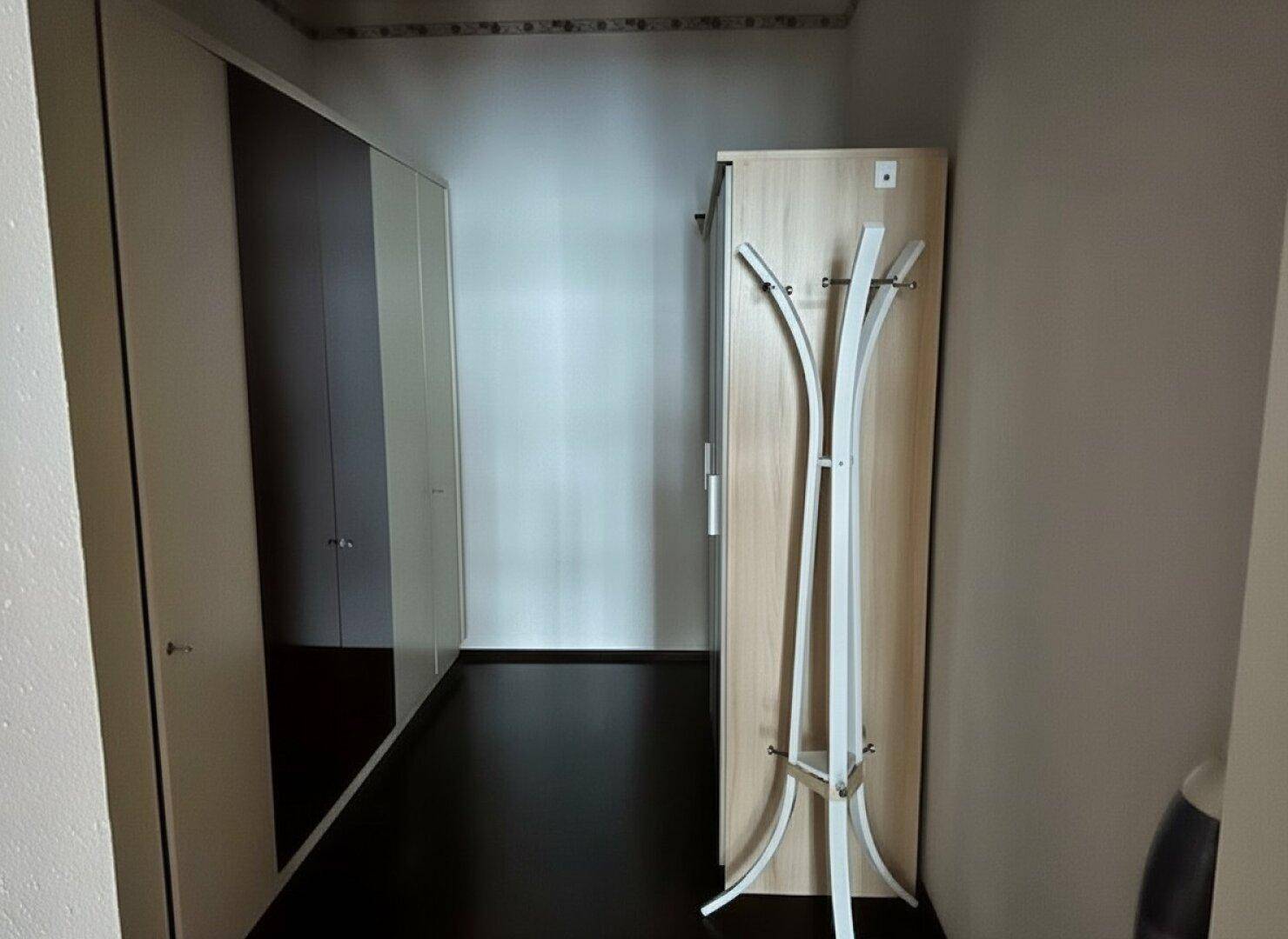 Heller Flur mit dunklem Fliesenboden, Einbauschränken und einem modernen Garderobenständer.