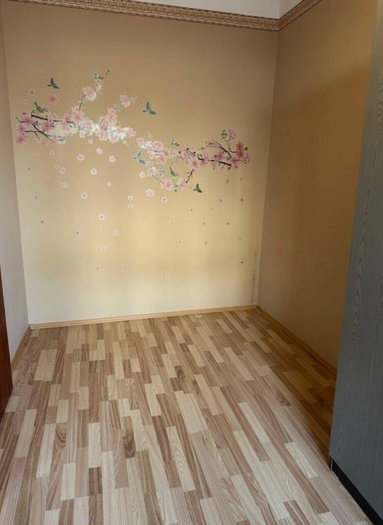 Helles Zimmer mit Laminatboden und einer dekorativen Blumenwandverzierung.