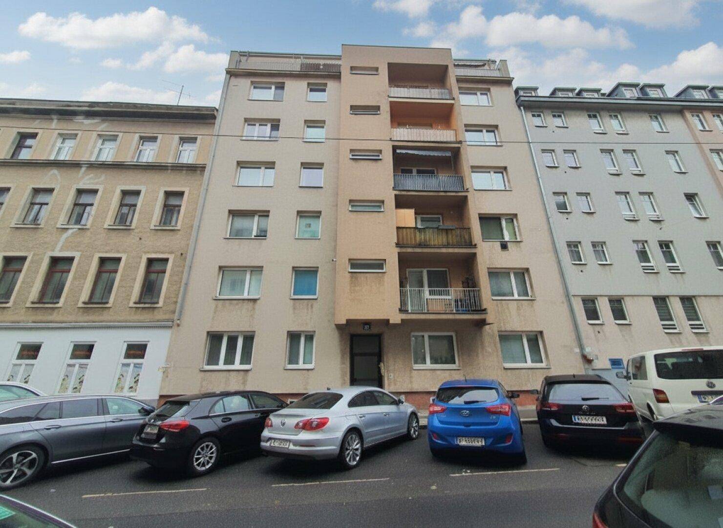 Mehrstöckiges Wohngebäude mit Balkonen und parkenden Autos auf der Straße.