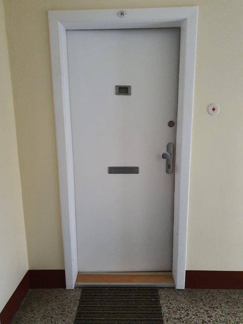 Wohnungseingangstür im Treppenhaus mit Gegensprechanlage und Fußmatte.