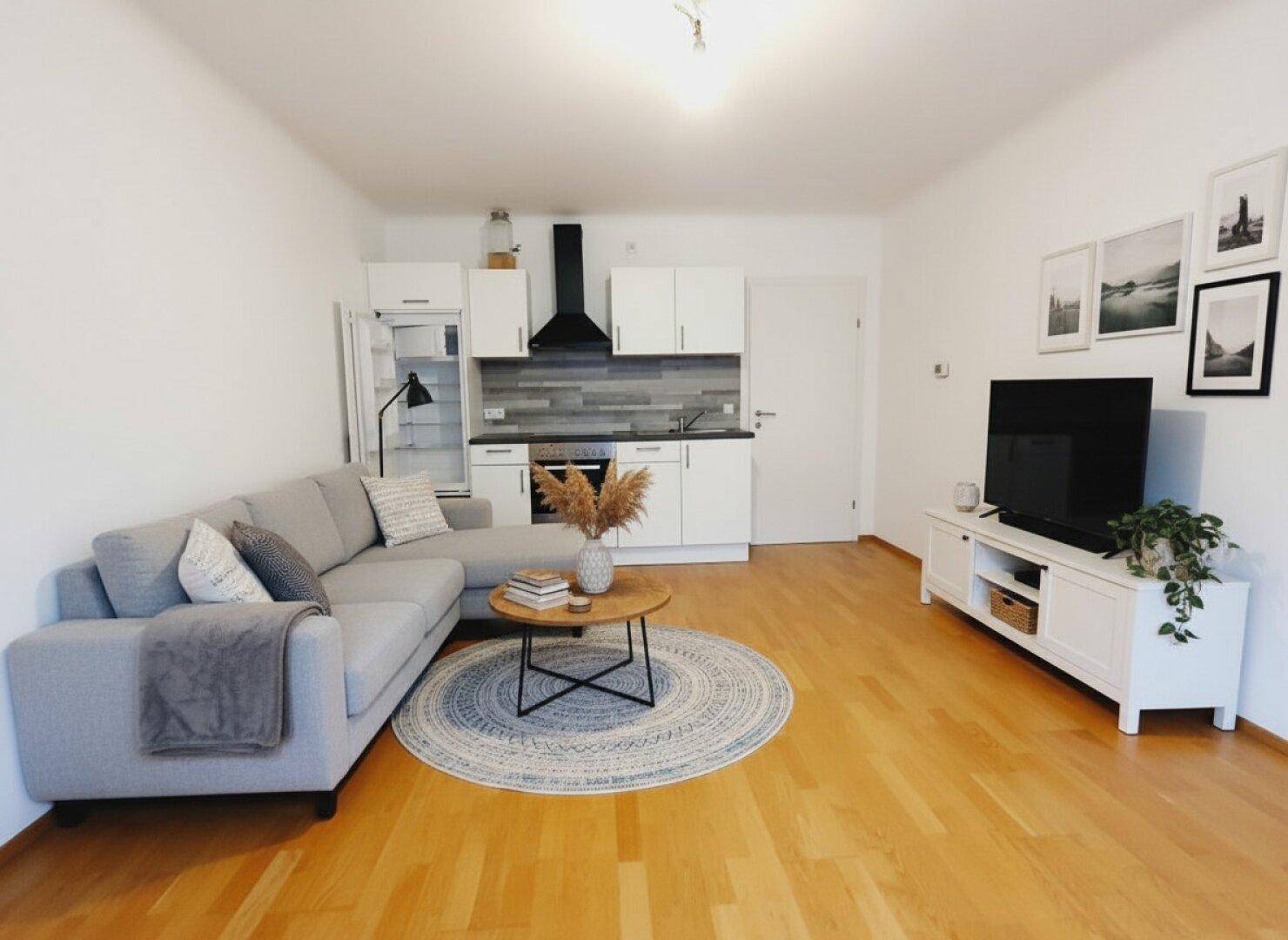 Gemütlicher Wohnbereich mit Ecksofa, Couchtisch und offener Küchenzeile im Hintergrund.