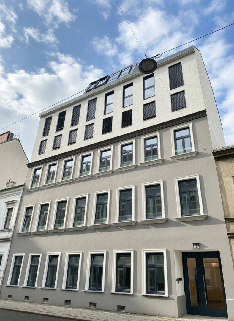 Modernes Mehrfamilienhaus mit heller Fassade, vielen Fenstern und Rollläden.