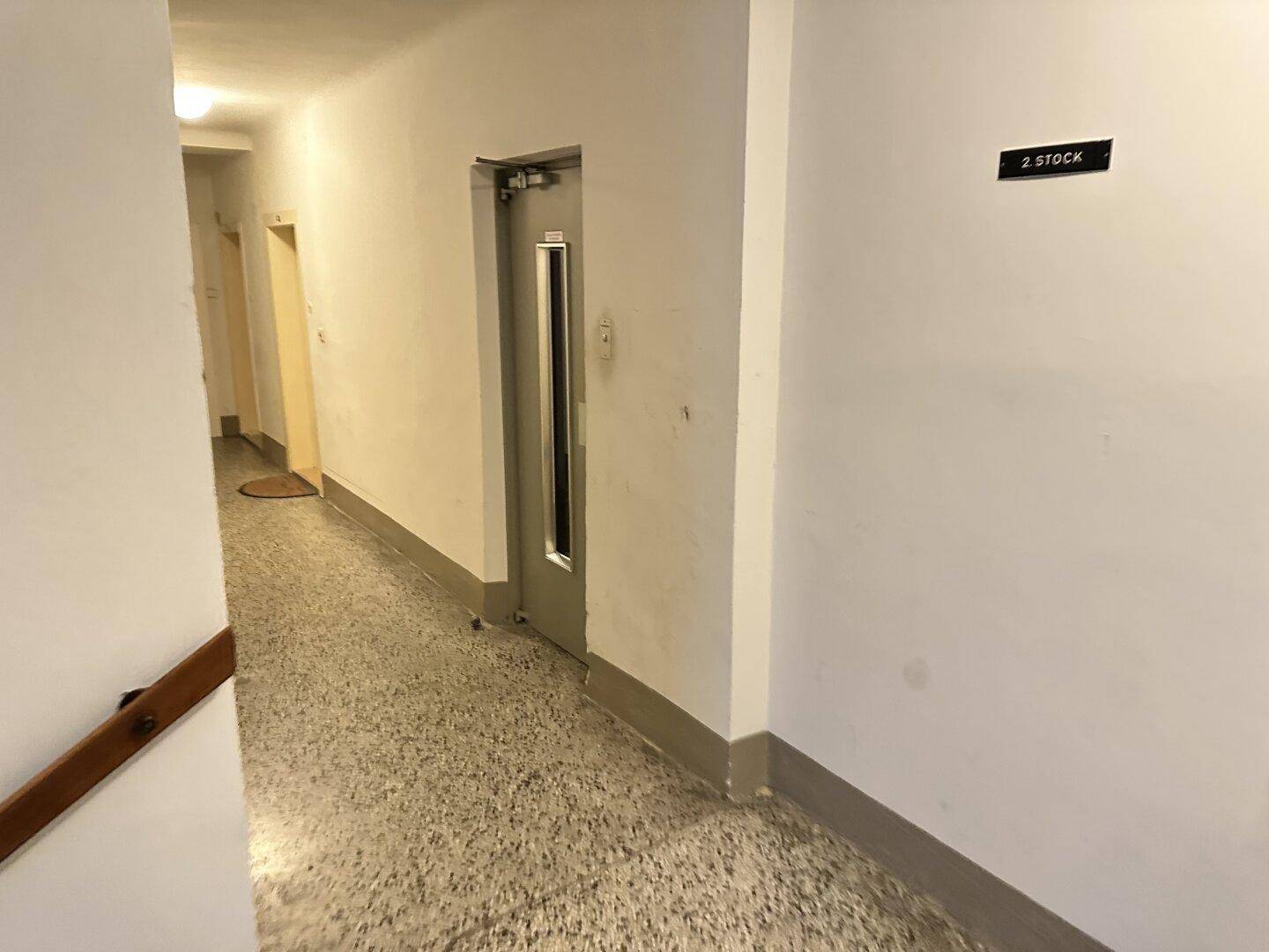 Heller Hausflur im zweiten Stock mit Terrazzoboden und Aufzugstür.