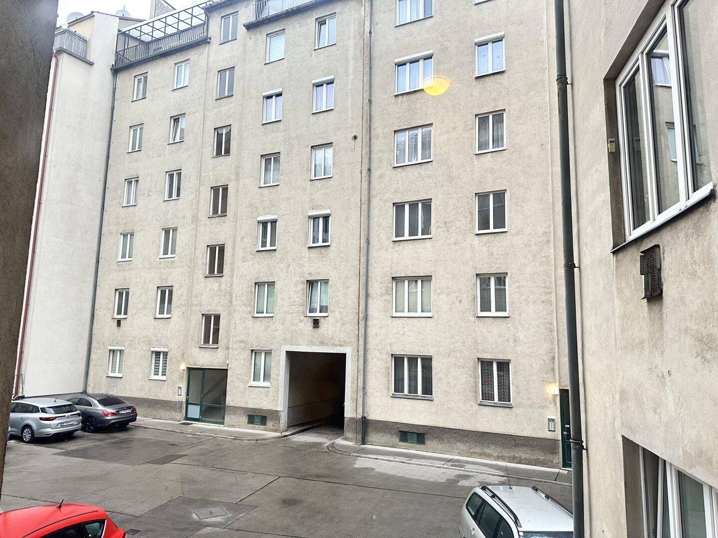Ansicht eines Mehrfamilienhauses von einem Innenhof mit geparkten Autos.