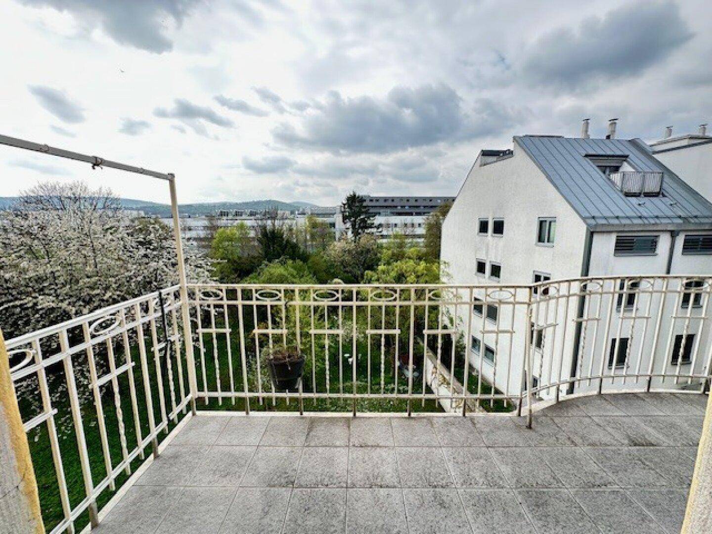Geräumiger Balkon mit Fliesenboden und schmiedeeisernem Geländer, bietet einen grünen Ausblick.