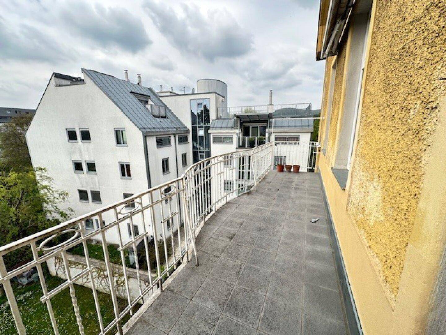 Langer, geschwungener Balkon mit Fliesenboden und Blick auf umliegende Gebäude und Bäume.
