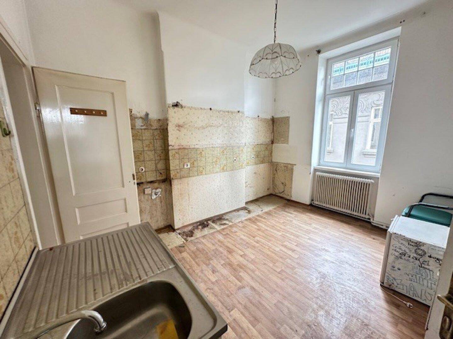 Renovierungsbedürftige Küche mit alten Fliesen, Spülbecken und einem Fenster für Tageslicht.