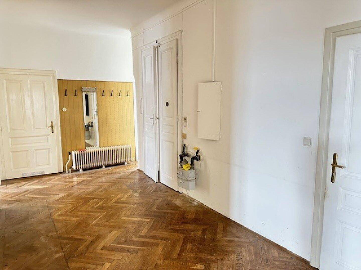 Flur mit Fischgrätparkett, Spiegel, Garderobe und Heizkörper, mit sichtbarem Gaszähler.