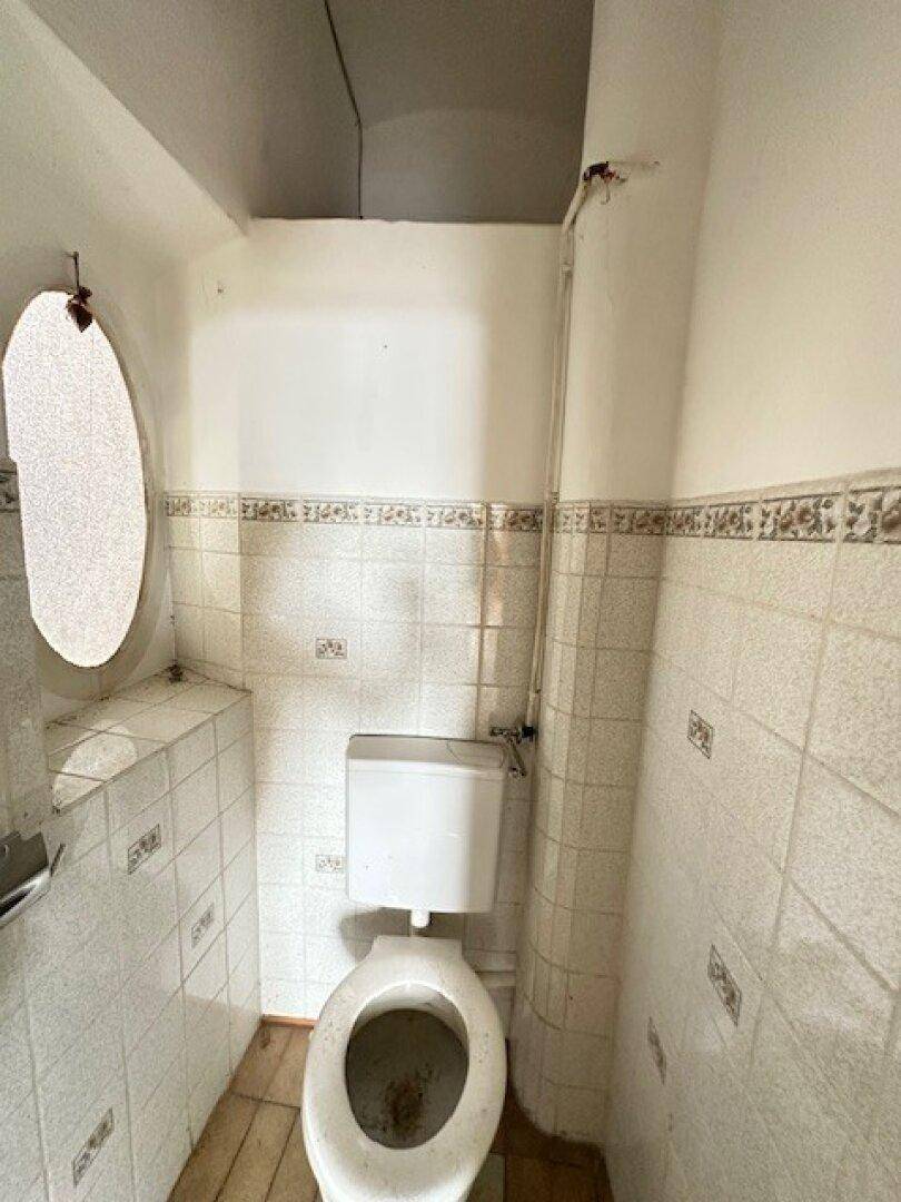 Kleines WC mit Toilette, gefliesten Wänden und einem ovalen Spiegel oder Fenster.