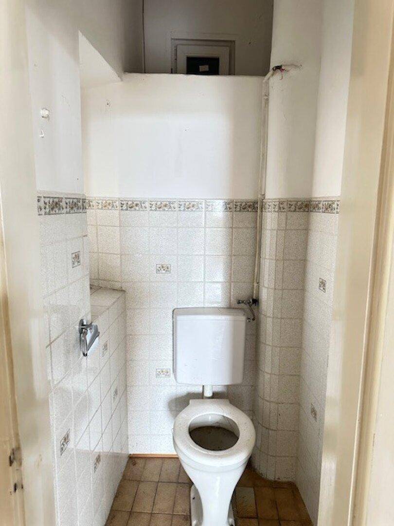 Kleines WC mit Toilette und gefliesten Wänden, in einem einfachen, funktionalen Zustand.