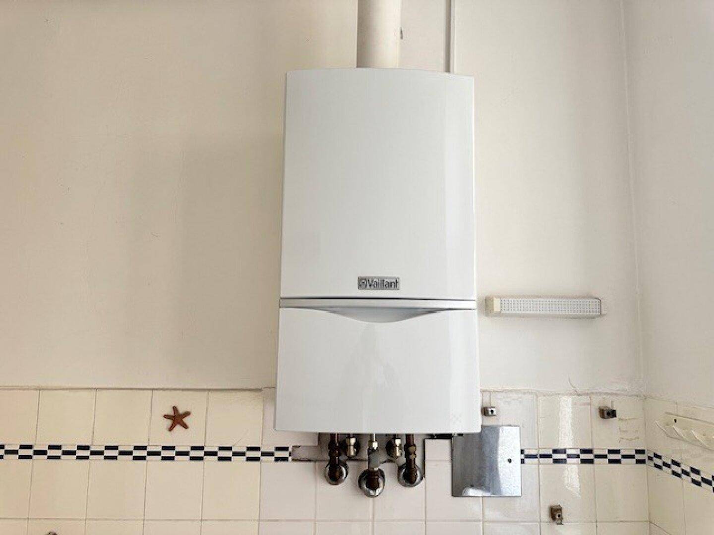 Nahaufnahme eines wandmontierten Vaillant Heizkessels über gefliesten Wänden im Badezimmer.