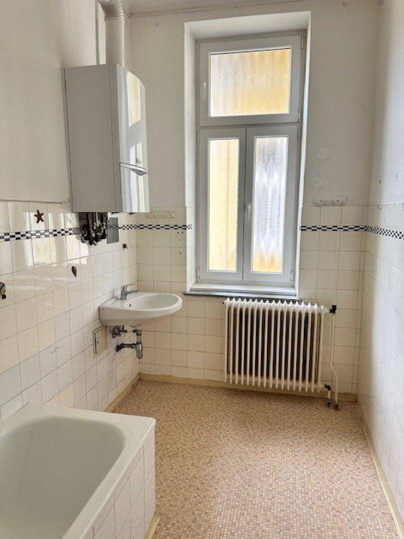 Badezimmer mit Badewanne, Waschbecken, Heizkörper und Fenster, mit Wandheizkessel.