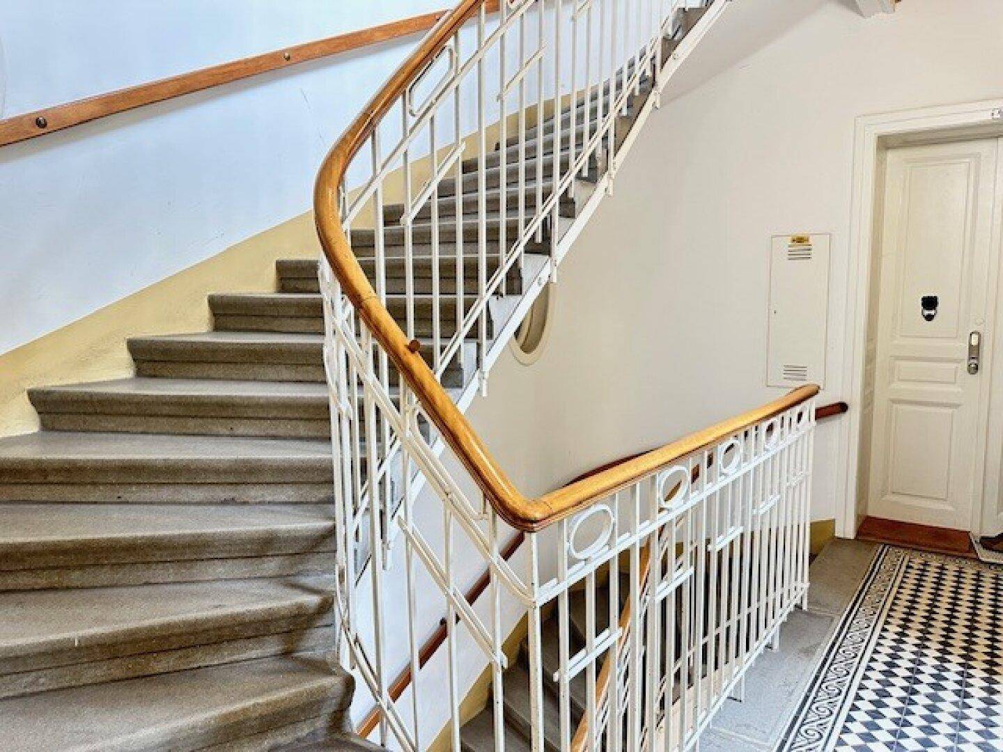 Geschwungenes Treppenhaus mit Steinstufen, Holzhandlauf und kunstvollem Metallgeländer in einem Altbau.