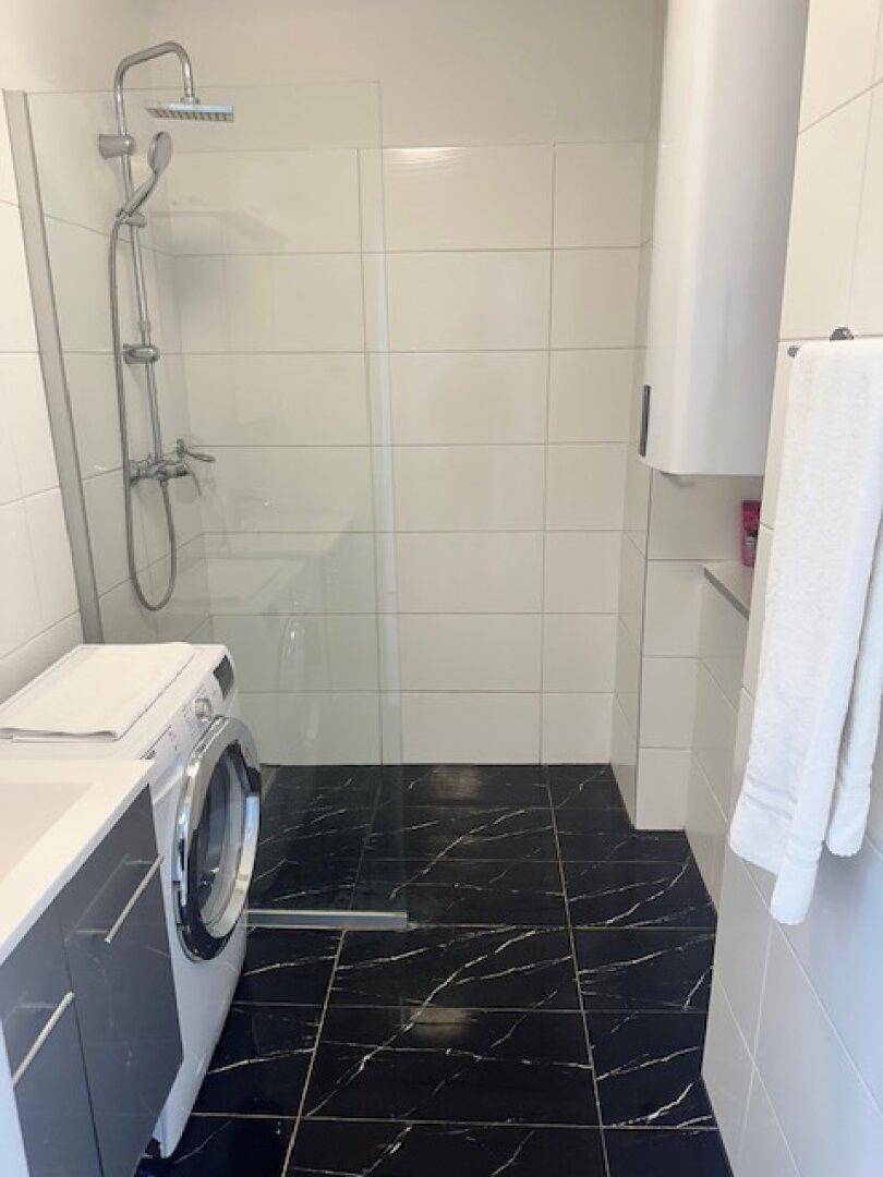 Modernes Badezimmer mit ebenerdiger Dusche, Waschmaschine und schwarzen Fliesen.